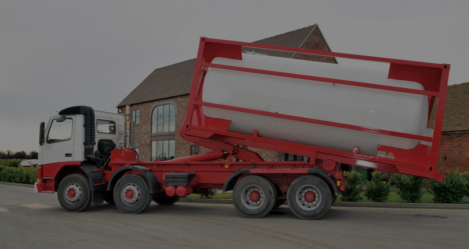 Red holding tank being delivered on a hook-lift trailer